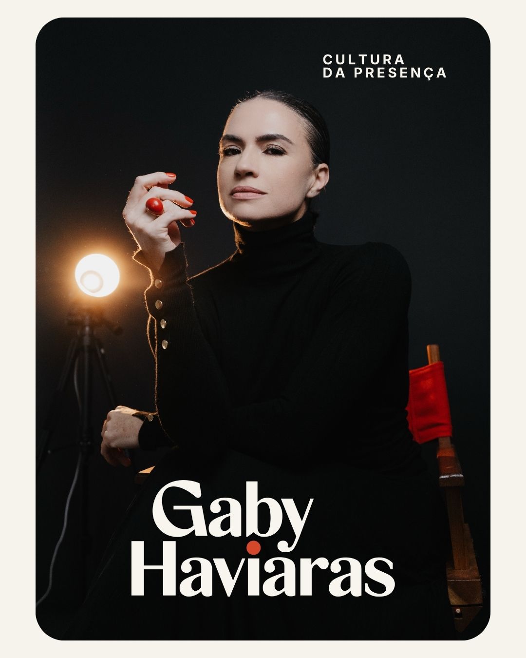 Gaby Haviaras, Cultura da Presença. Gaby de preto, sentada ao lado de um refletor e de uma cadeira de diretora vermelha.