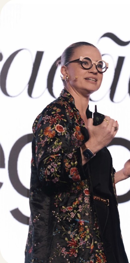 Gaby Haviaras no palco, de microfone, diante de um telão com a palavra comunicação.
